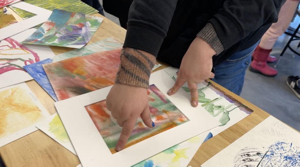 Sam adjusts a framing mat over a colorful painting.